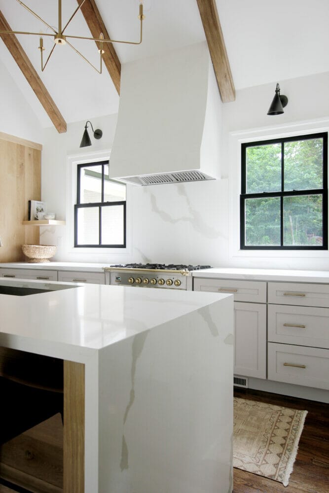 White farmhouse kitchen with Caesarstone's Calacatta Maximus on the kitchen counters and waterfall island, exposed beams, black window frames, and dark floors.
