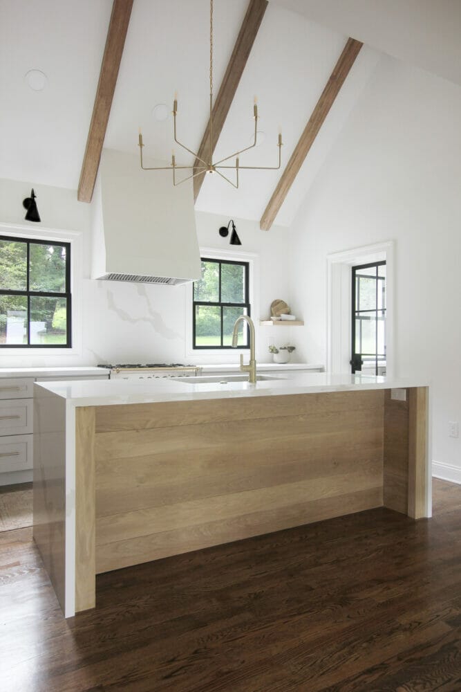White farmhouse kitchen with Caesarstone's Calacatta Maximus on the kitchen counters and waterfall island, exposed beams, black window frames, and dark floors.